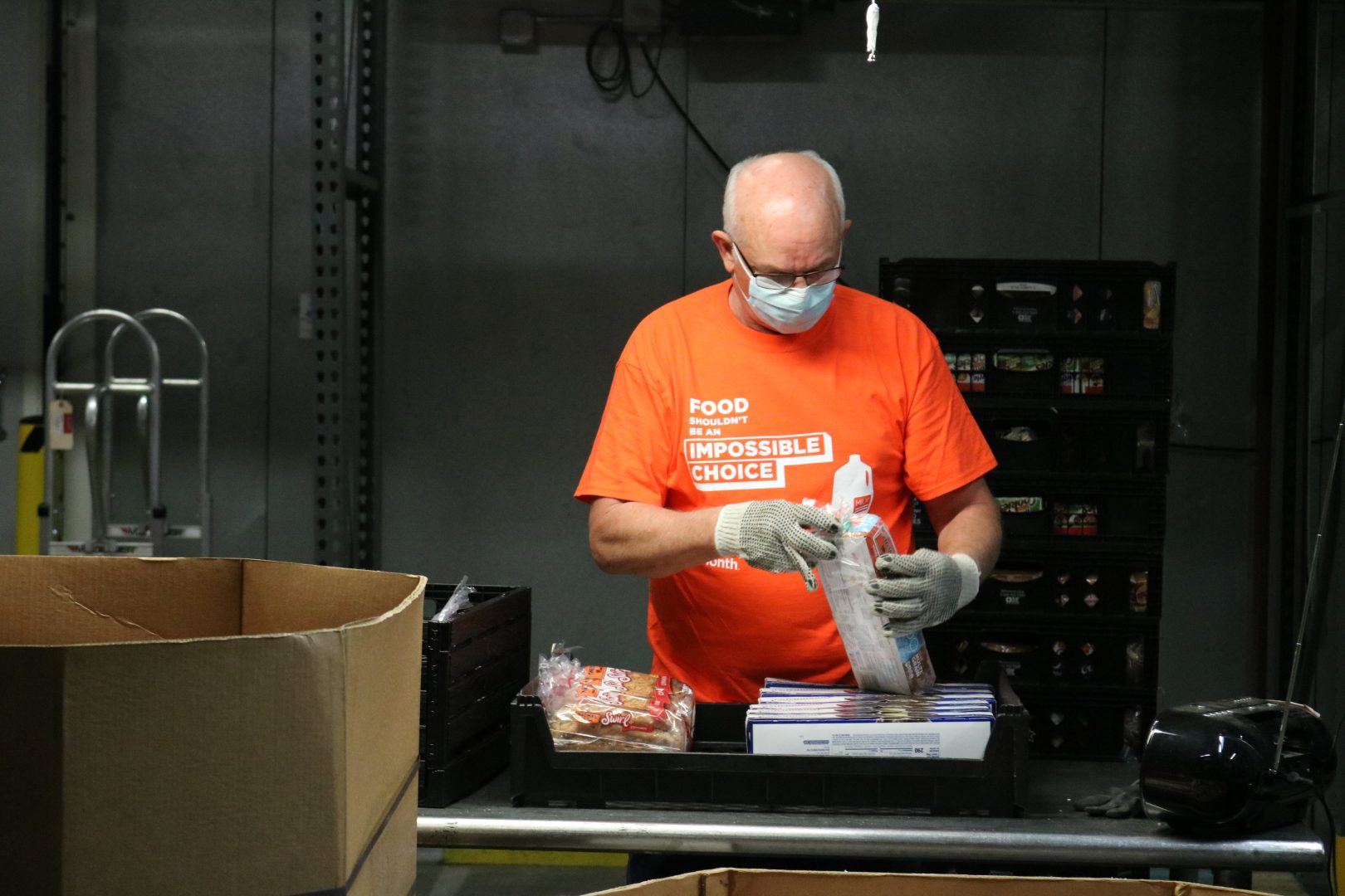 A man in an orange shirt and mask diligently works on a box