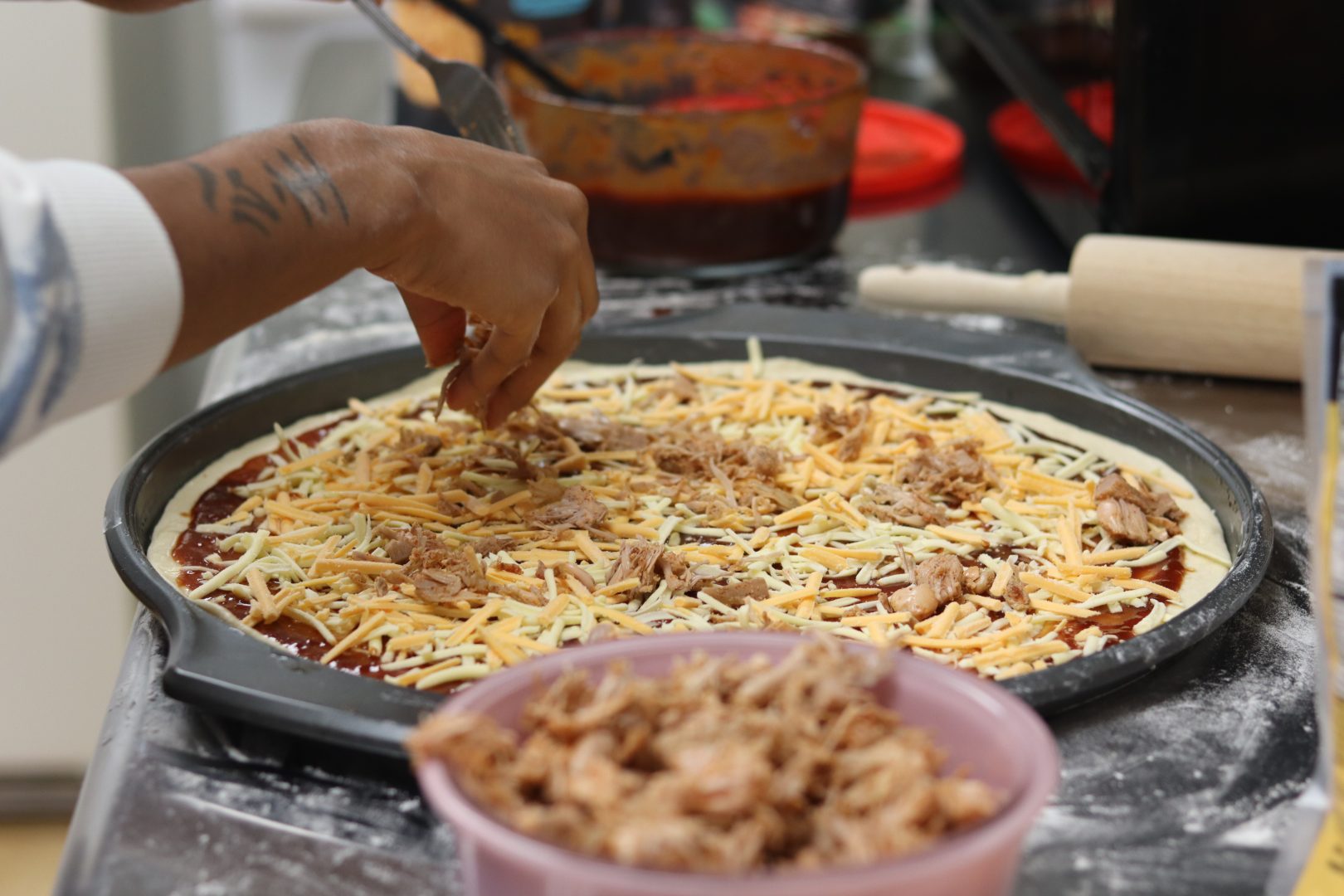 Daijah, Community Cook. Hand sprinkling vegan cheese on pizza.